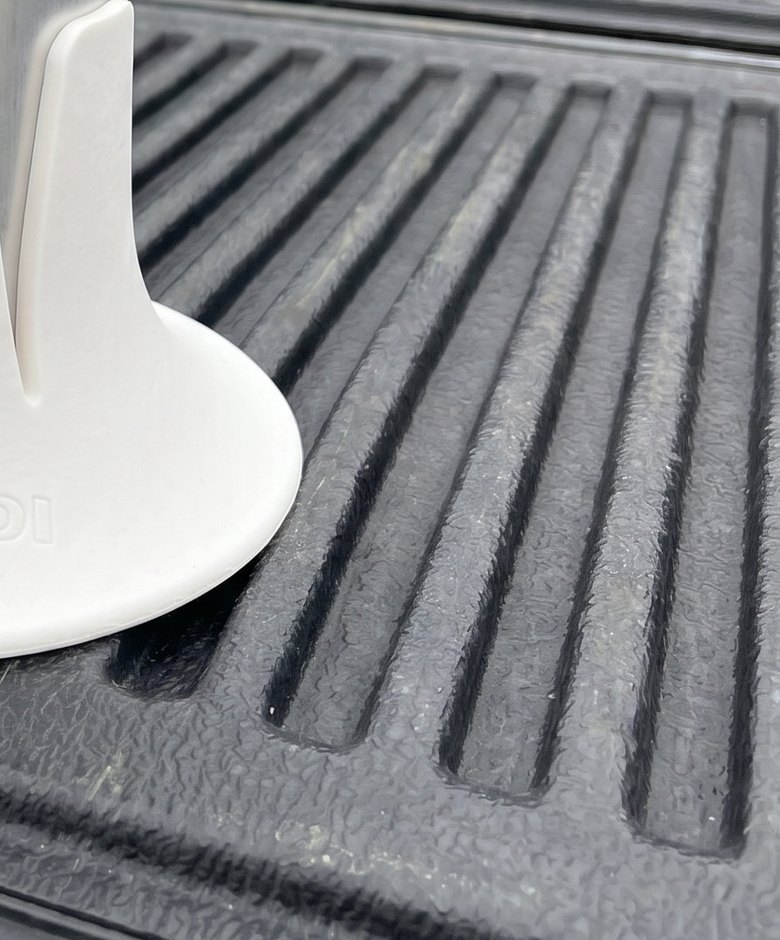Close-up of a white Steadi base sitting across the ribs of a textured black truck bed rail.
